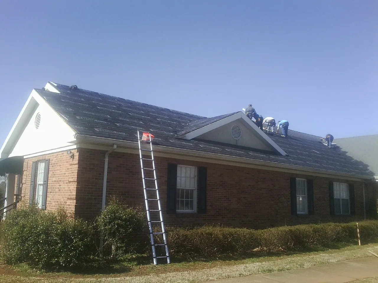 Crew tearing shingles off a brick ranch roof with a ladder set — Emergency Roof Repair work by our crew in Farley