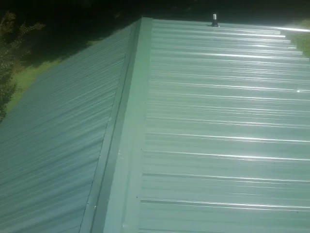 New green metal panels meeting at the ridge of a roof — Flat Roof Repair work by our crew in Farley