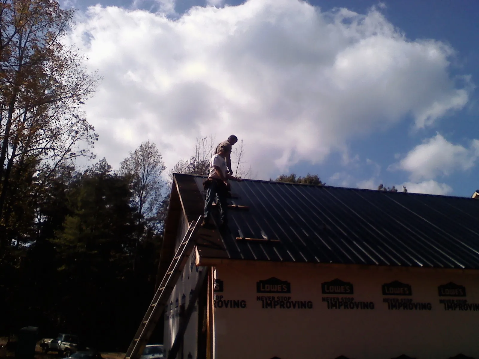 Roofer fastening dark metal panels high against a cloudy sky, from a Roof Inspection job in Farley