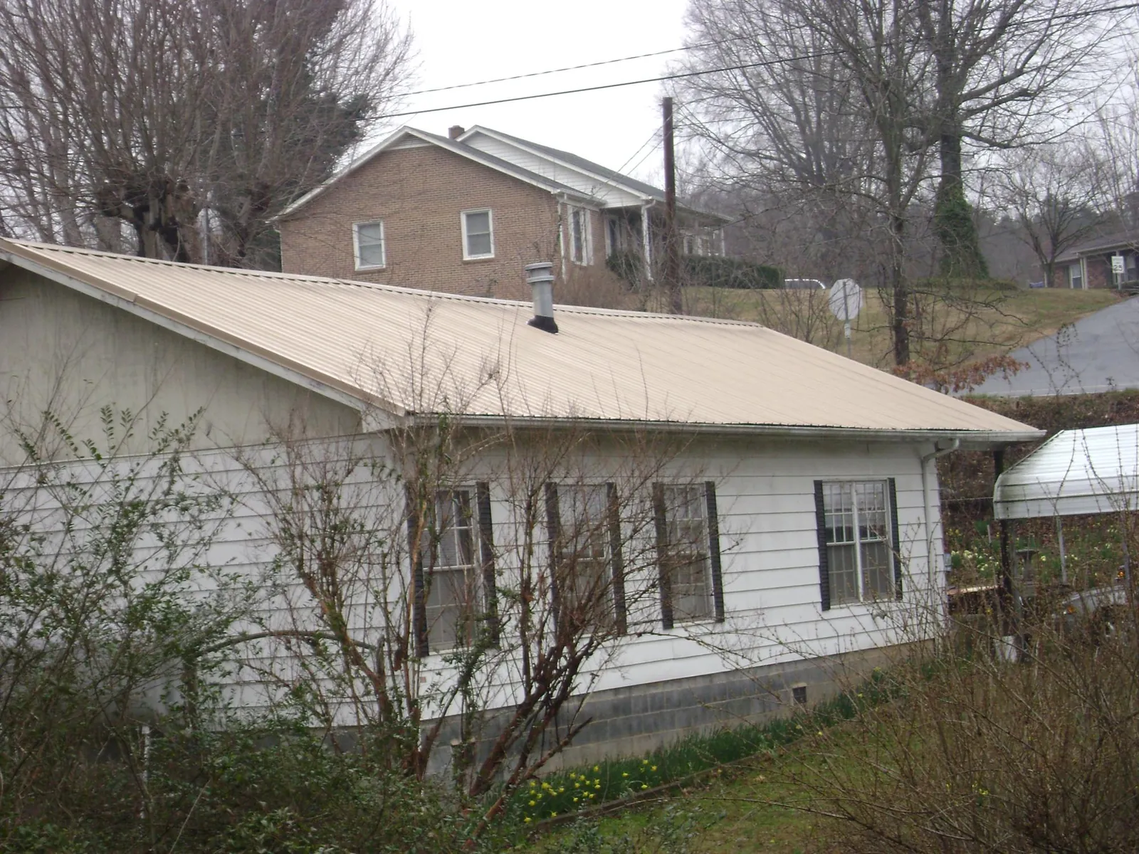 Tan metal roof on a white sided house set into a hillside — Commercial Roofing by Roofing Brothers in Farley