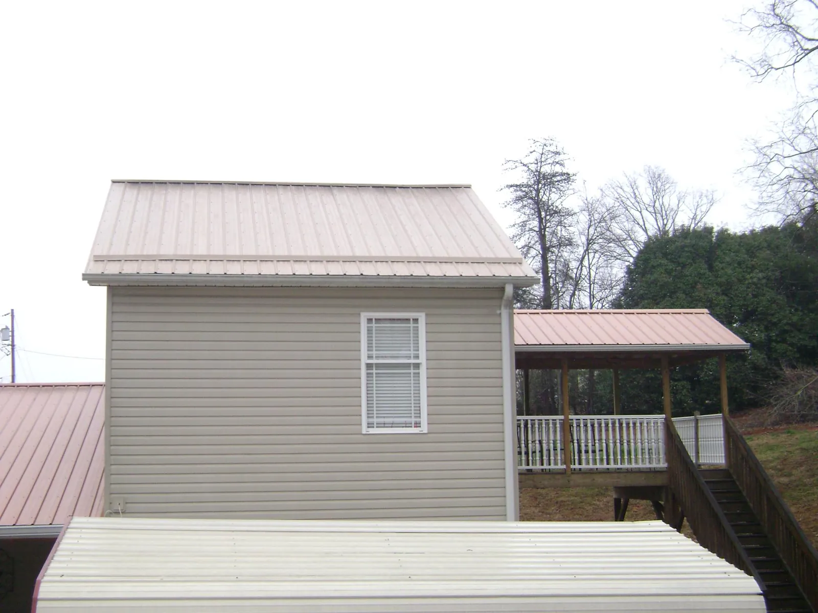 Tan metal roofs on a two story addition and attached porch, from a Roof Replacement job in Farley